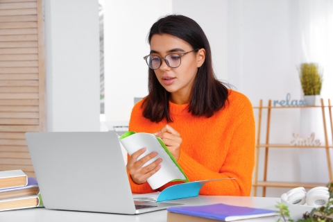 Zdjęcie przedstawia młodą kobietę uczącą się online. Trzyma notatnik i aktywnie uczestniczy w lekcji przy laptopie, co symbolizuje naukę poprzez działanie i praktykę. Skupienie na twarzy sugeruje zaangażowanie w proces edukacyjny. Dzięki regularnym ćwiczeniom i praktycznym metodom nauki możesz szybciej przyswajać wiedzę i rozwijać swoje umiejętności językowe.